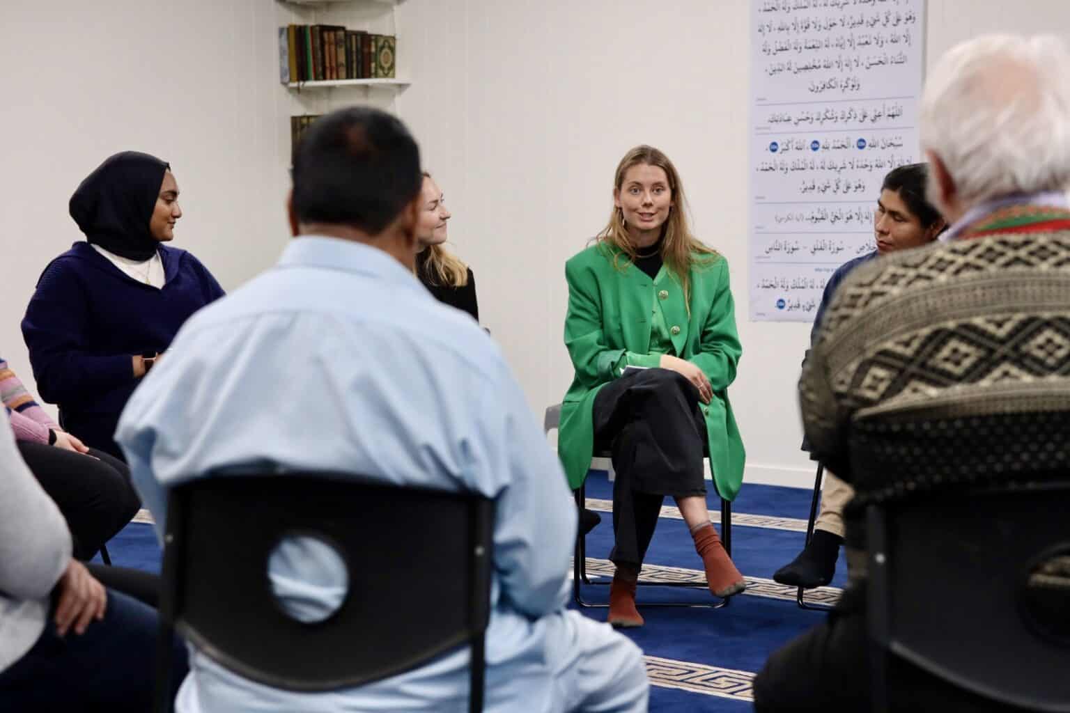 en kvinne kledd i grønt samtaler med menn og kvinner av ulike religioner